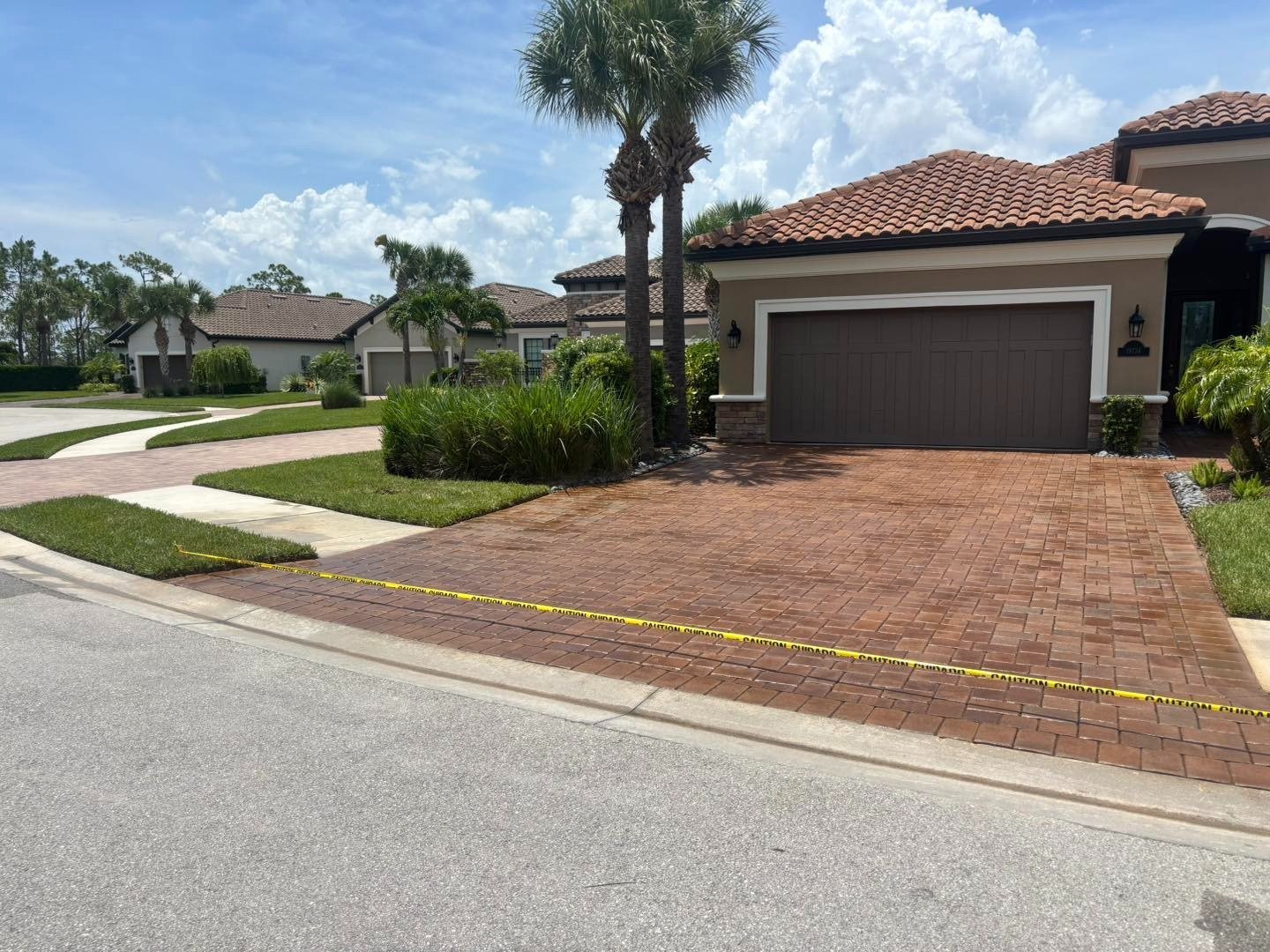 Red paver driveway bordered by caution tape outside a home with palms