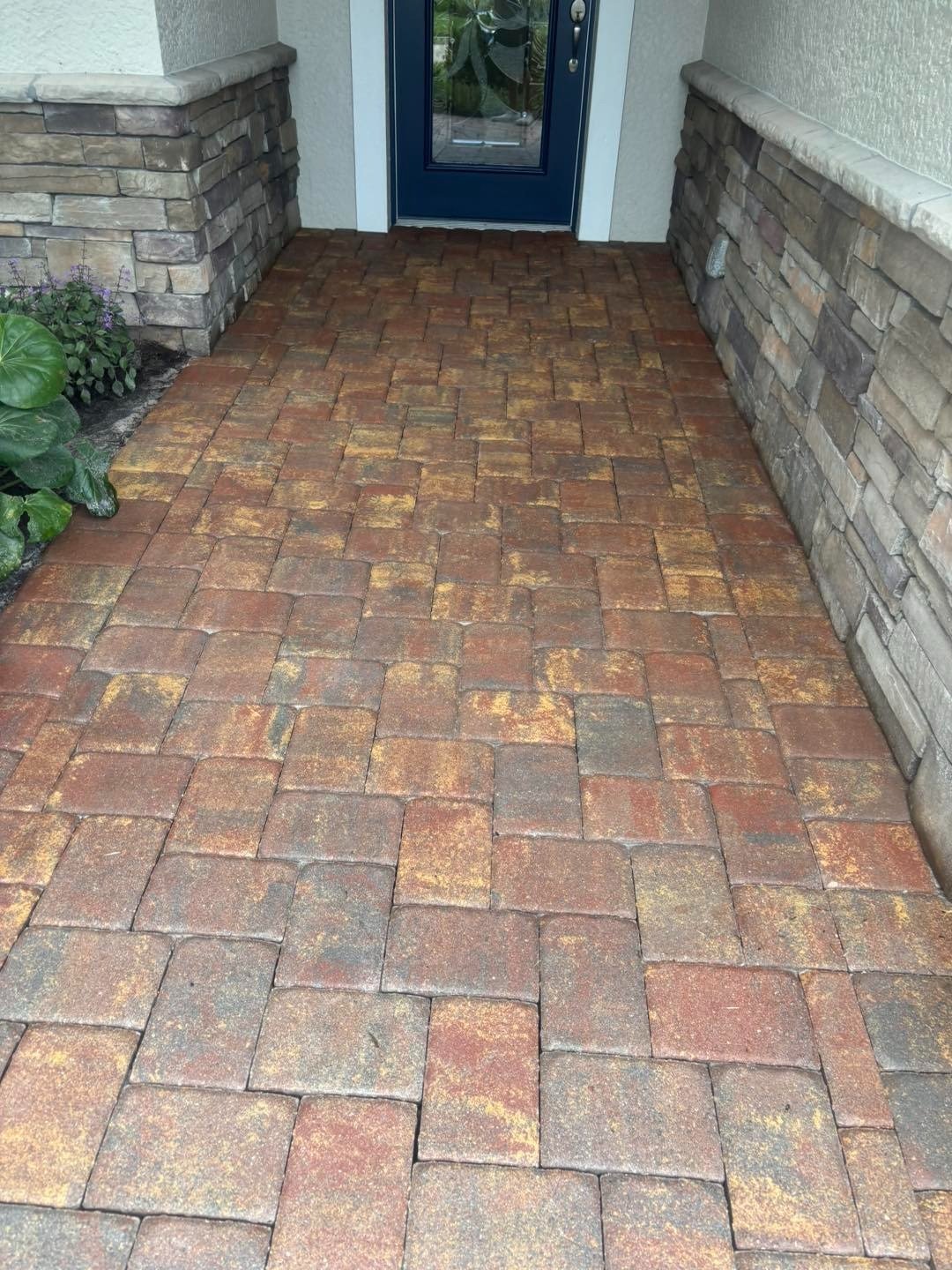 Reddish paver entryway leading to a blue door between stone-clad walls