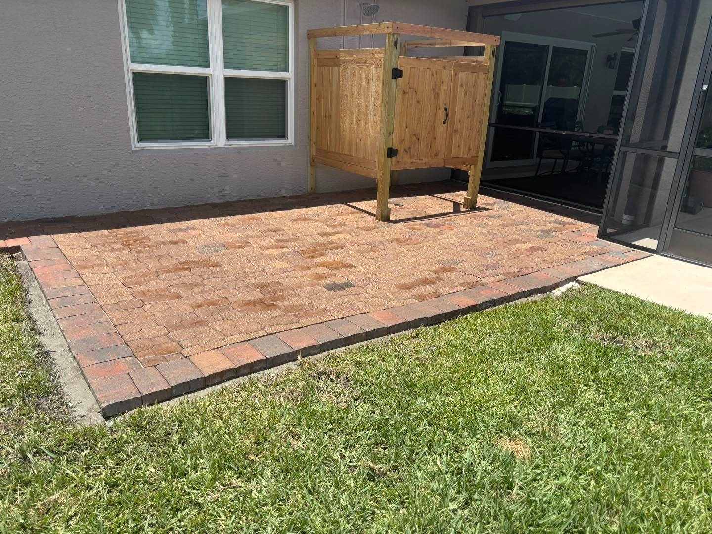 Reddish paver patio with dark border beside a wooden outdoor shower gate