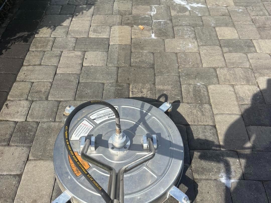 Round surface cleaning attachment resting on a gray paver driveway