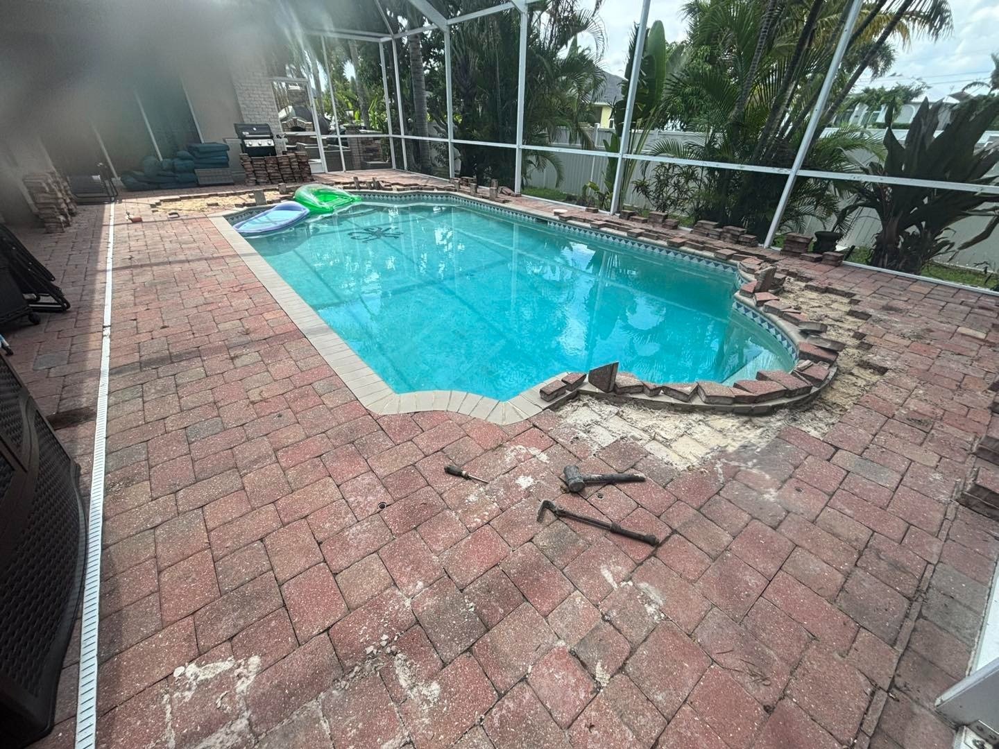 Screened swimming pool with loose pavers and displaced coping along the near edge