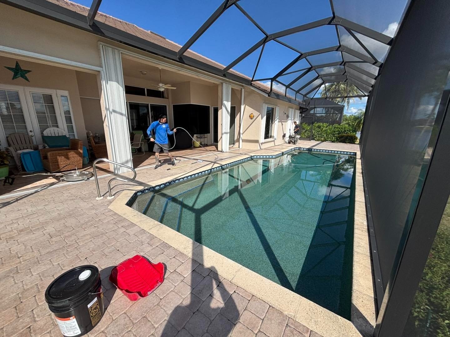 Screened swimming pool with paver surroundings and cleaning supplies on the deck