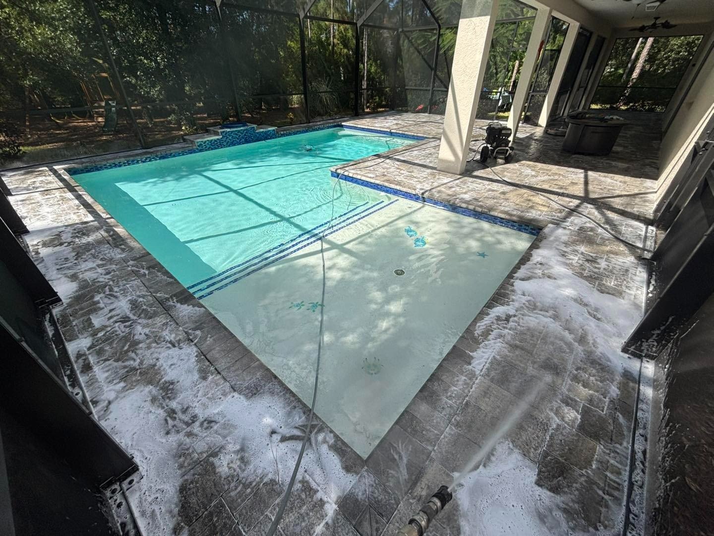 Screened swimming pool with patches of white foam across the adjoining paver deck