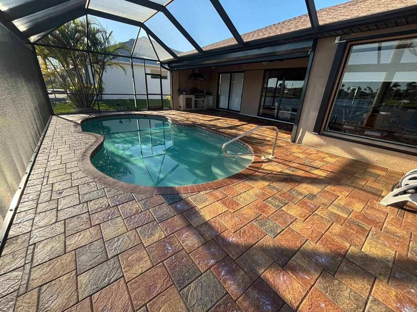 Screened pool with warm brown patterned decking and shaded patio seating