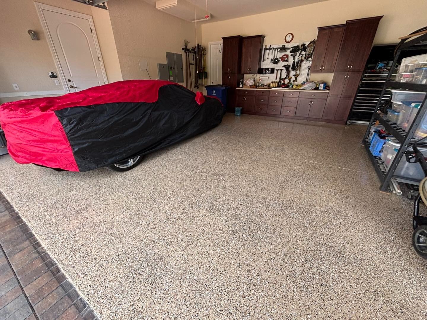 Speckled garage floor beside a covered car and storage cabinets