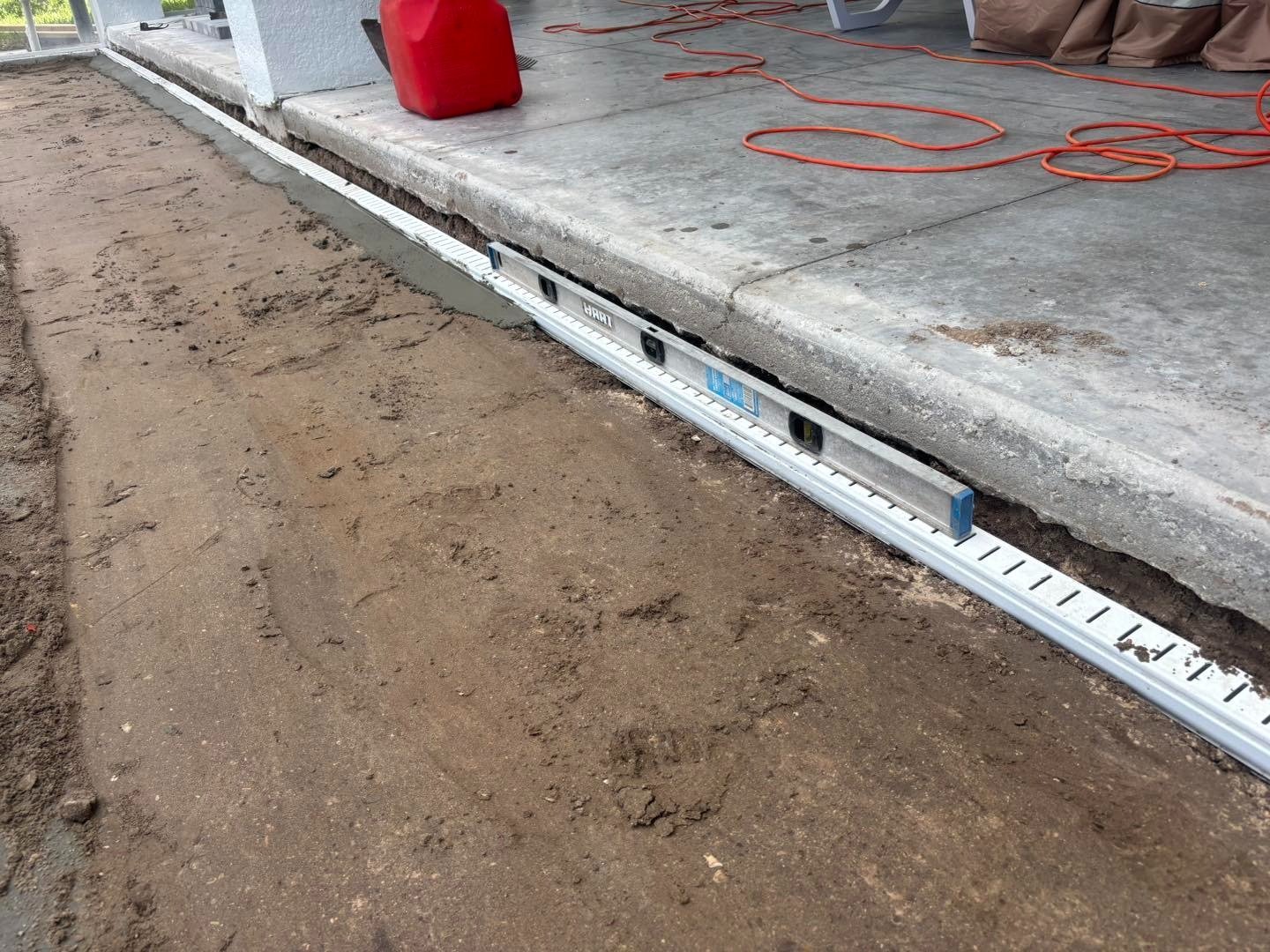 Long spirit level along a concrete patio edge beside an exposed sand bed