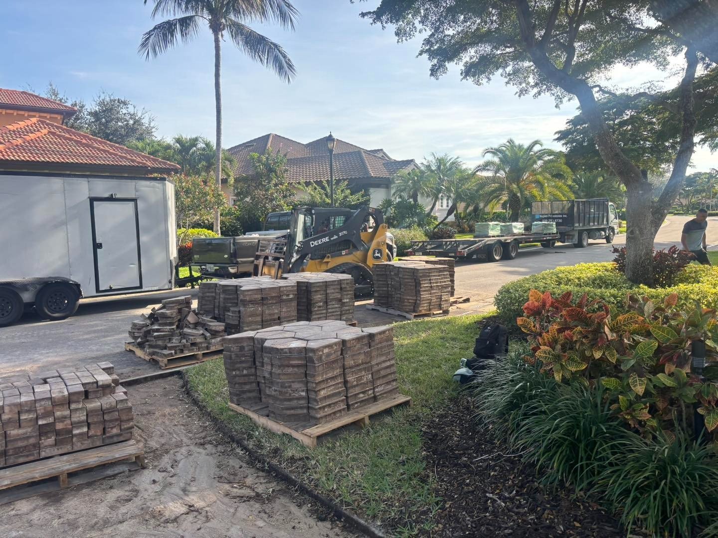 Stacks of paving blocks beside a driveway, trailer, and work equipment