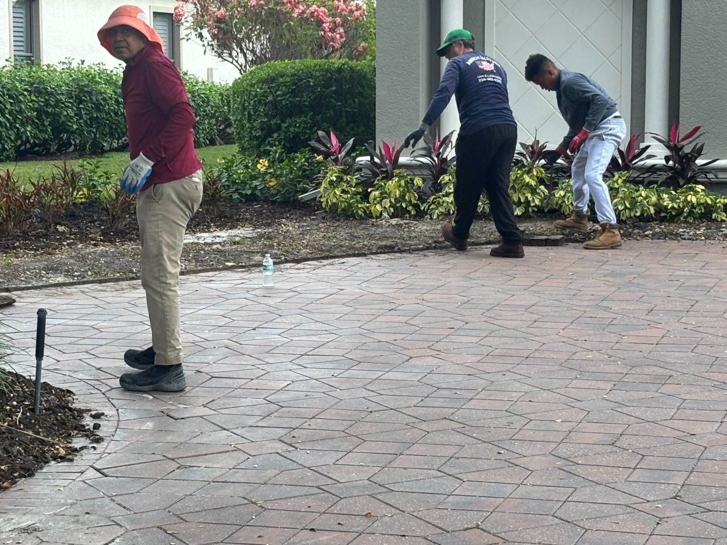 Three workers using tools along a landscaped paver driveway