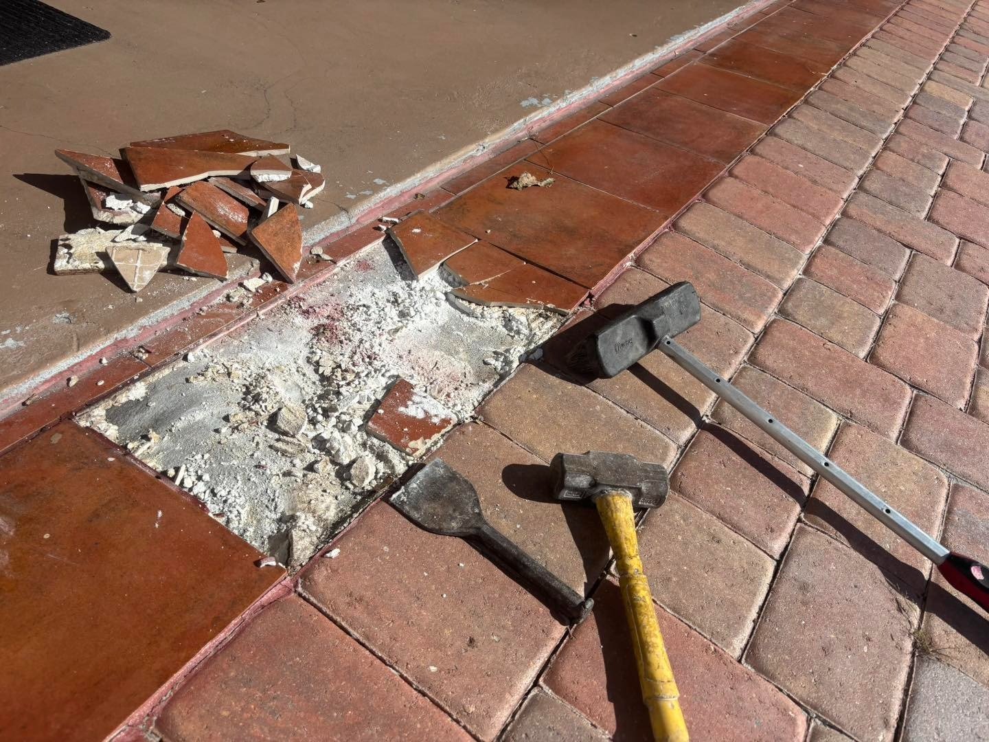 Tools and broken material beside removed red garage threshold pavers