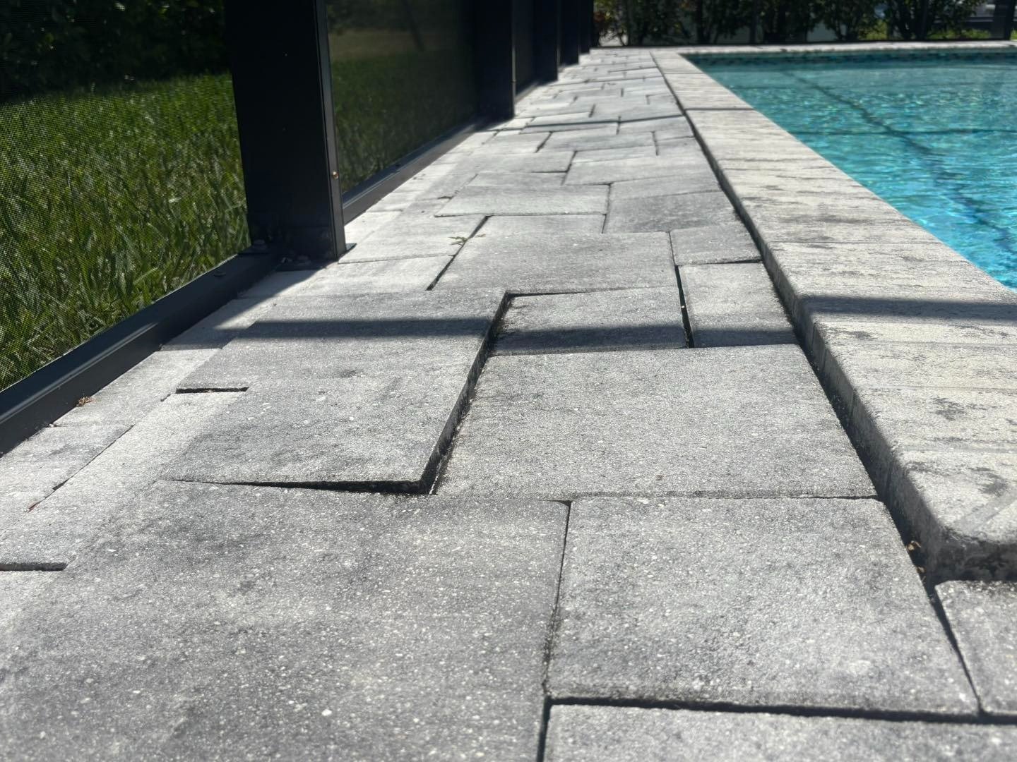 Uneven gray pool deck pavers with raised edges beside a screened enclosure