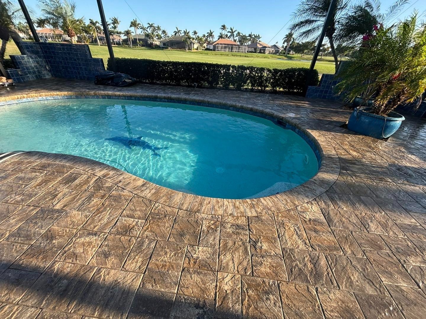 Warm brown patterned deck surrounding a screened pool overlooking a grassy landscape