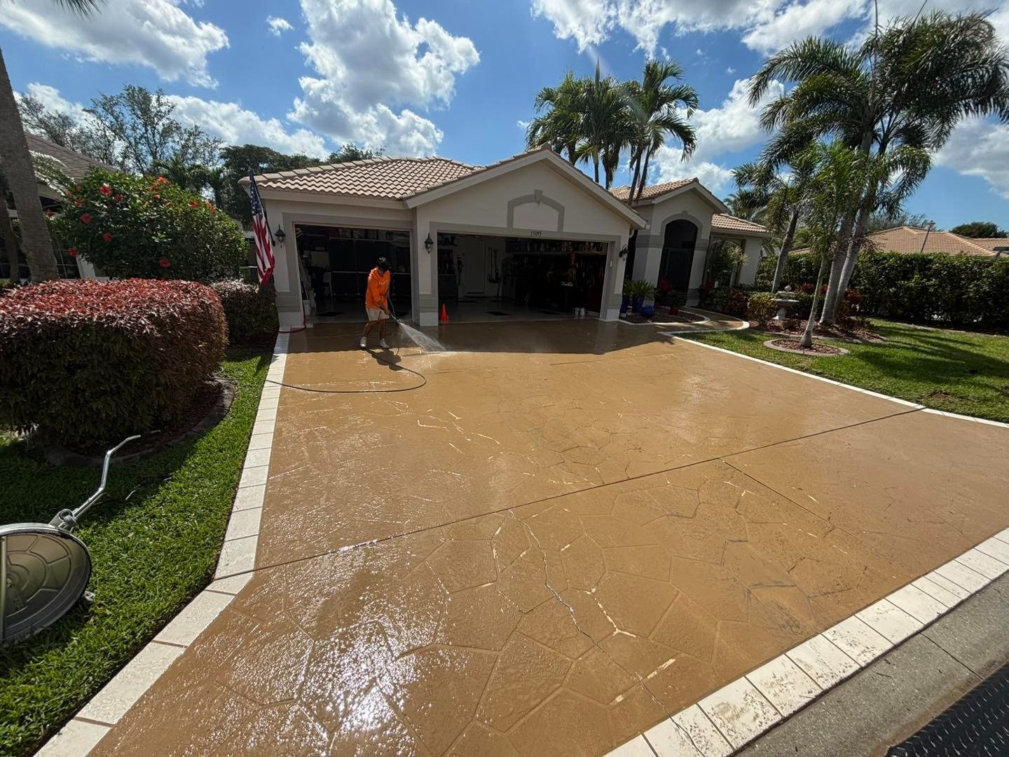 Wet brown driveway bordered by white pavers in front of a home