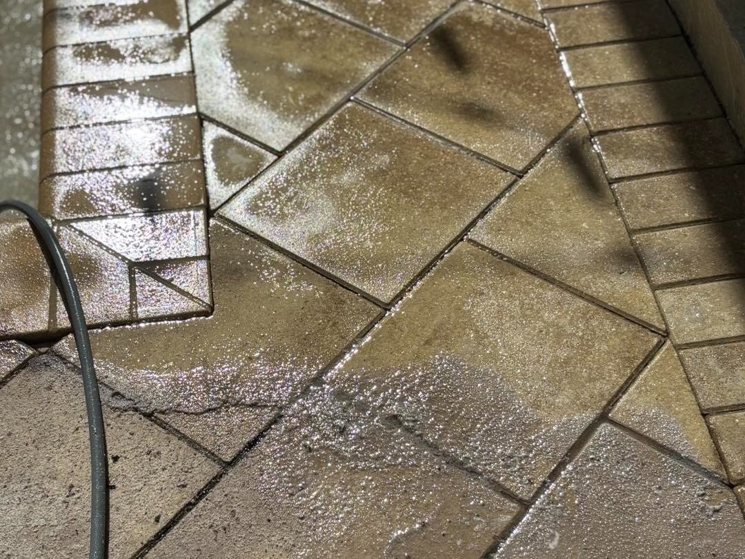 Wet brown patterned paving with hose along one edge