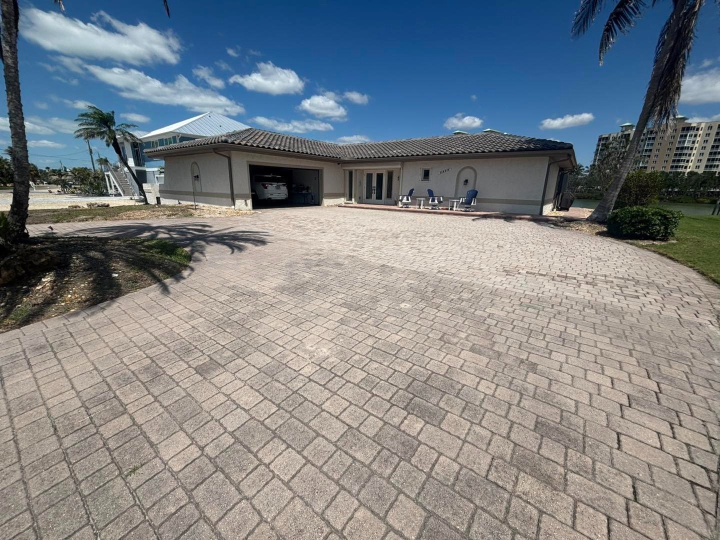 Wide gray paver driveway approaching a home with palms and landscaped edges