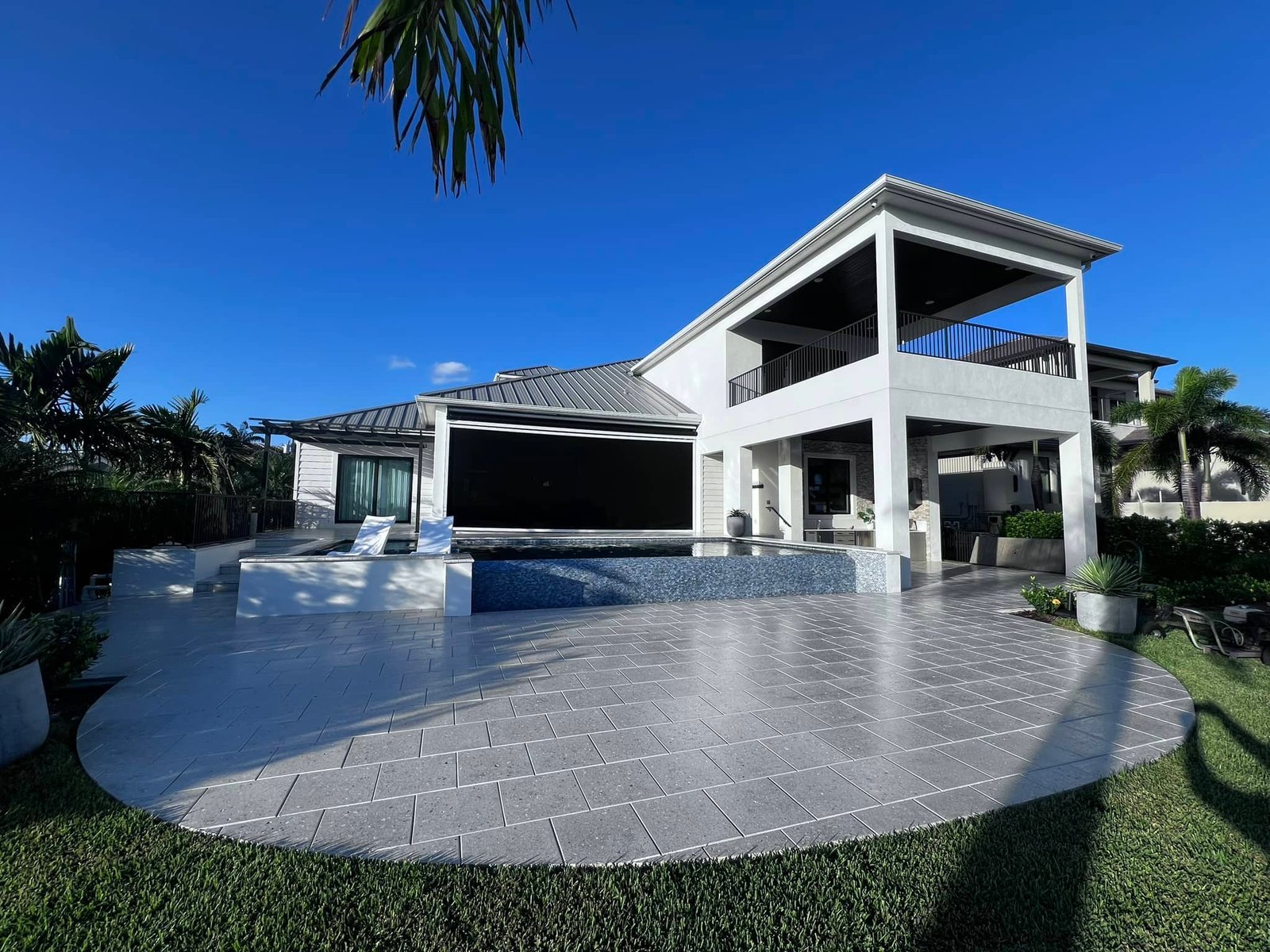 Wide pale pool deck outside a two-story waterfront home under blue sky