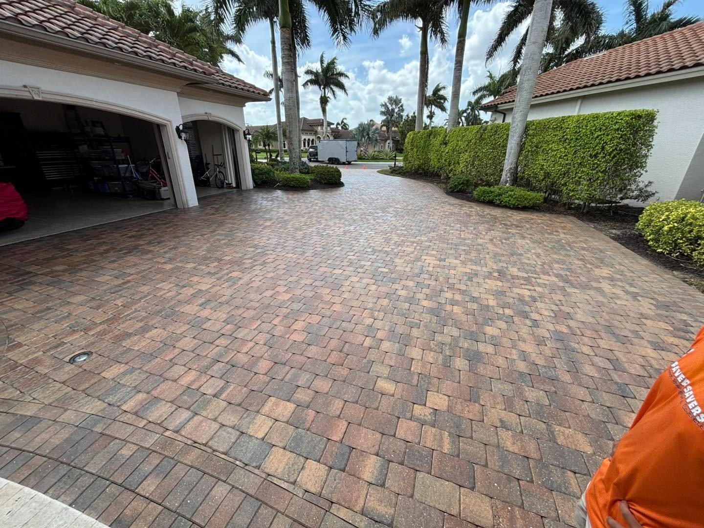 Wide paver driveway between an open garage and green hedge