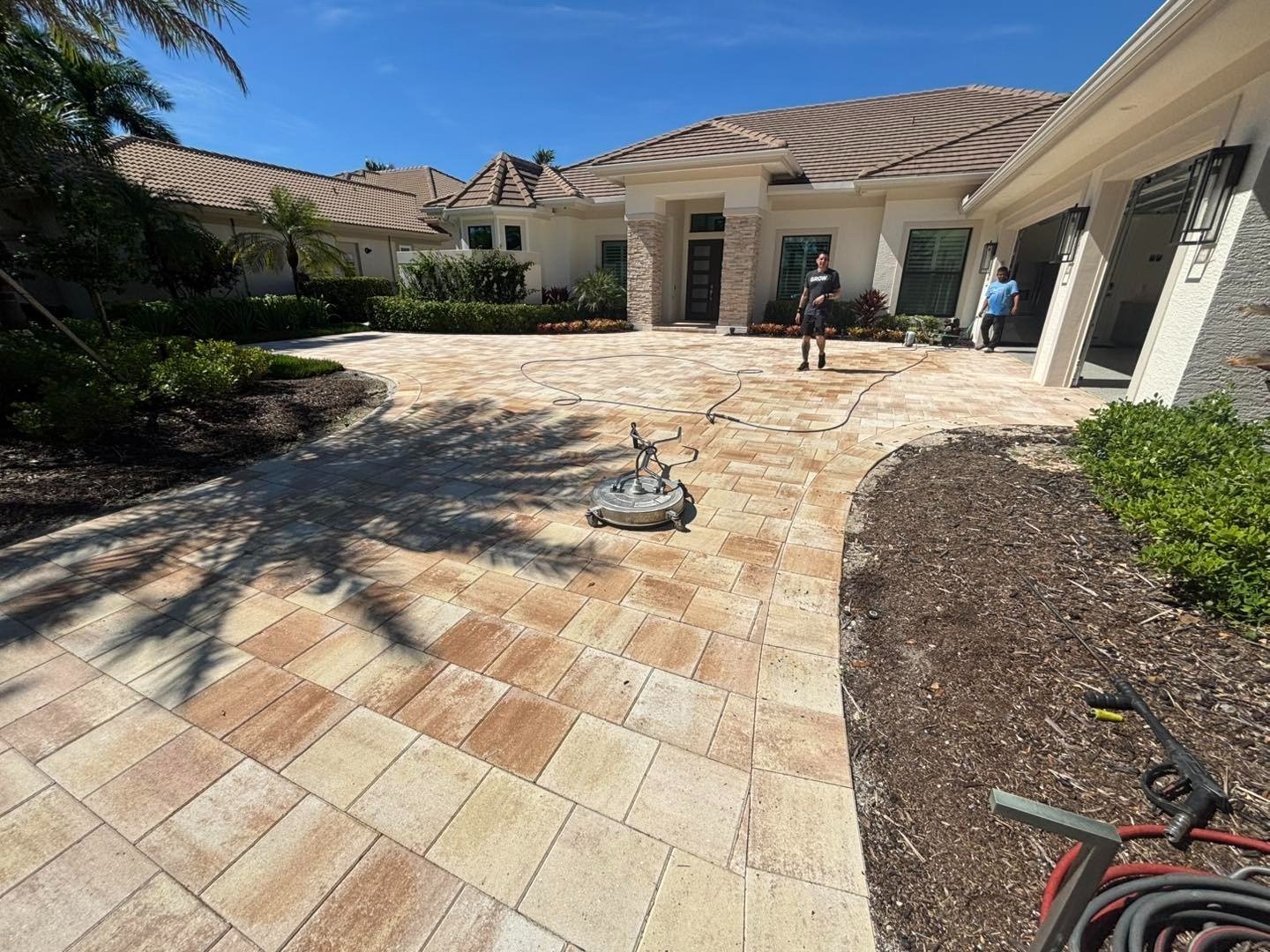 Wide view of a multicolored paver driveway with cleaning equipment and workers