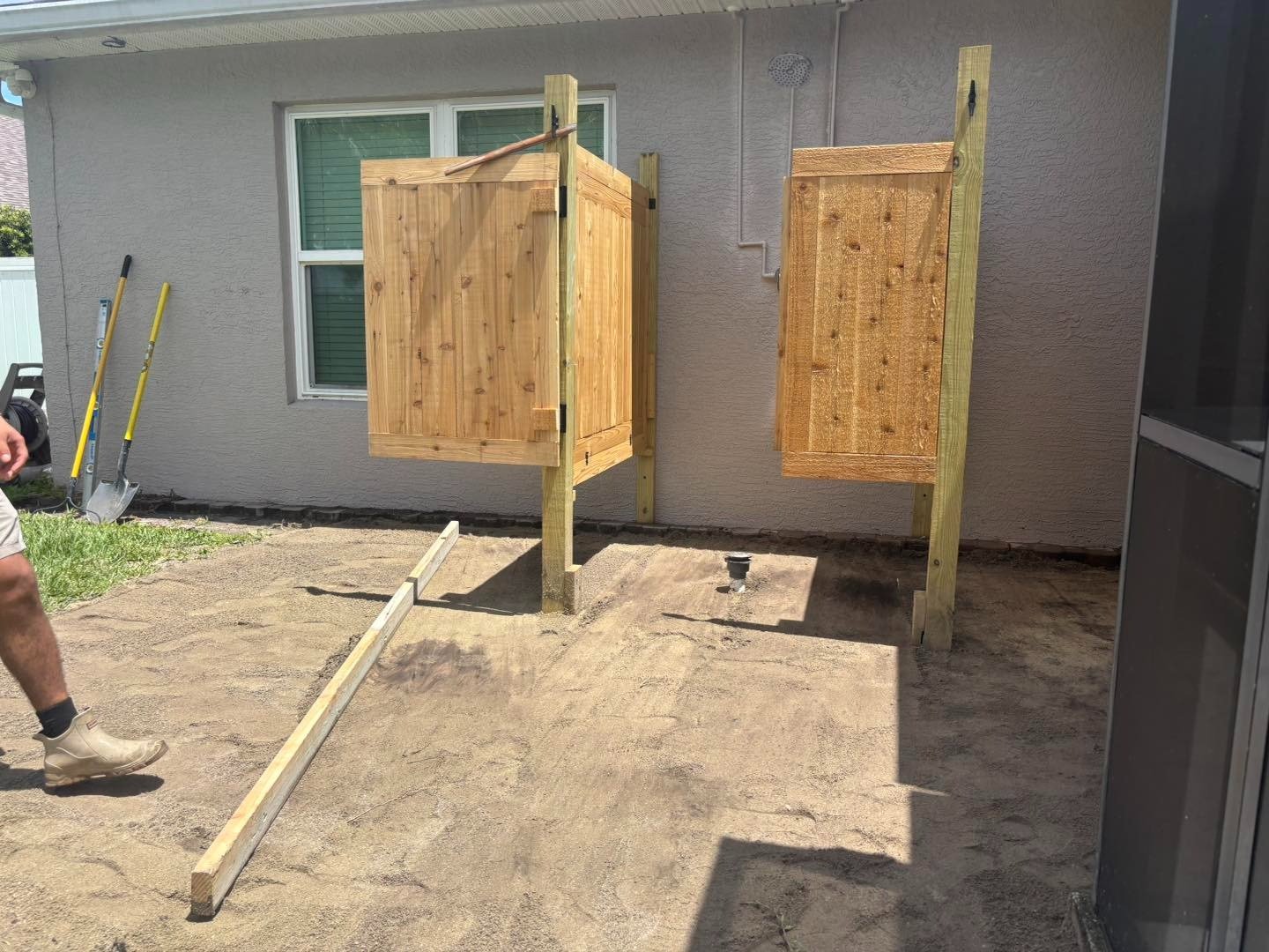 Wooden outdoor shower enclosure above exposed ground beside a house window