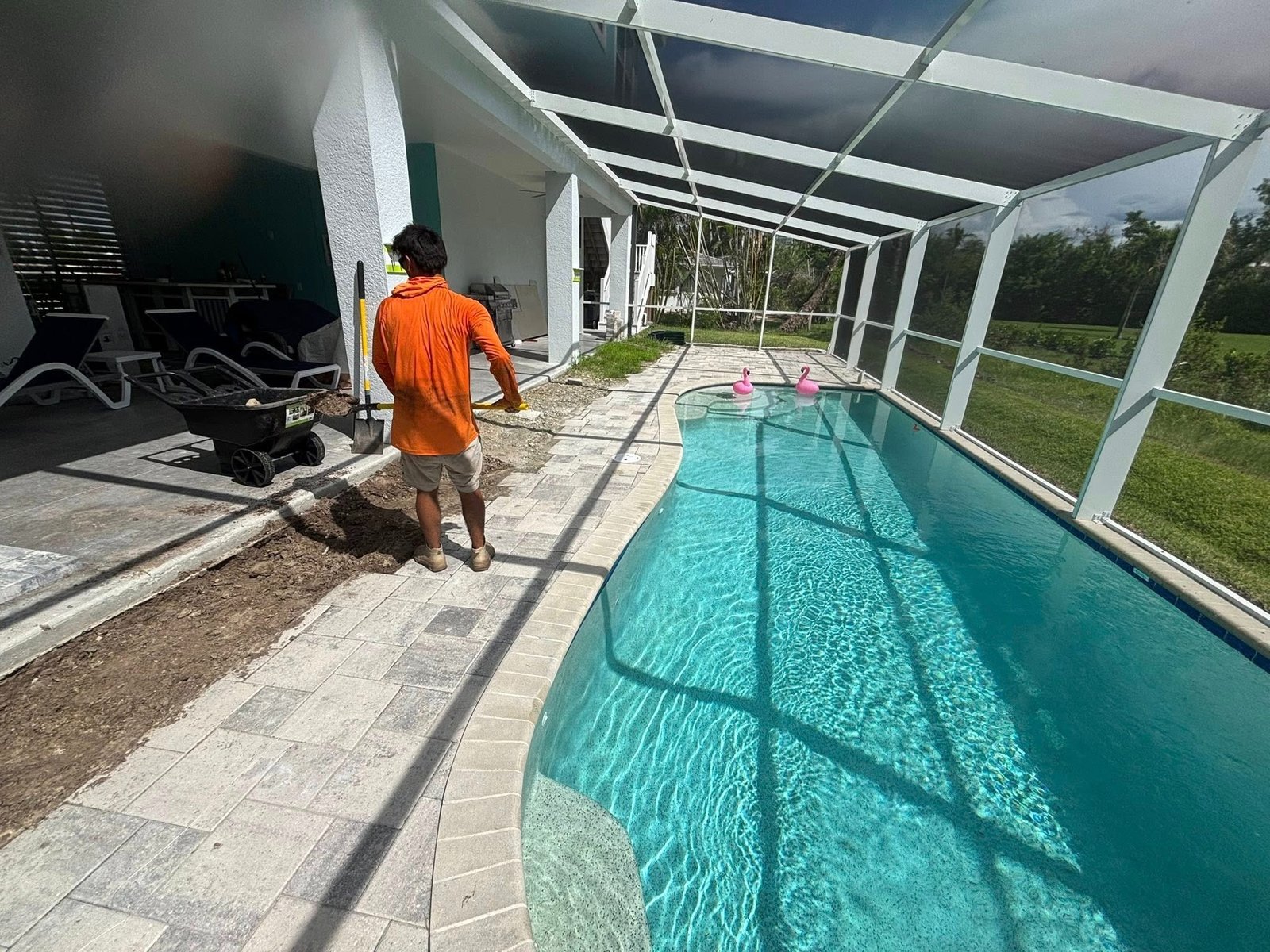 Worker beside a partially opened paver pool deck inside a screen enclosure