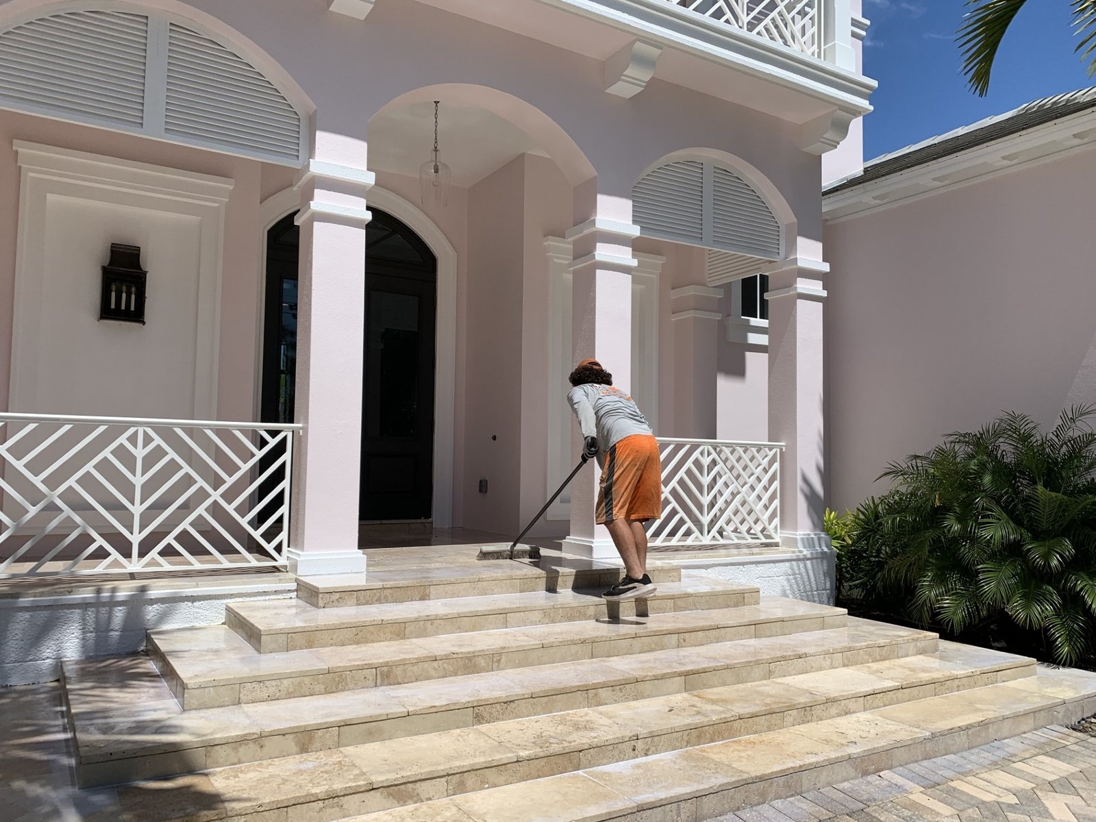 Worker cleaning front steps beneath a covered porch with columns