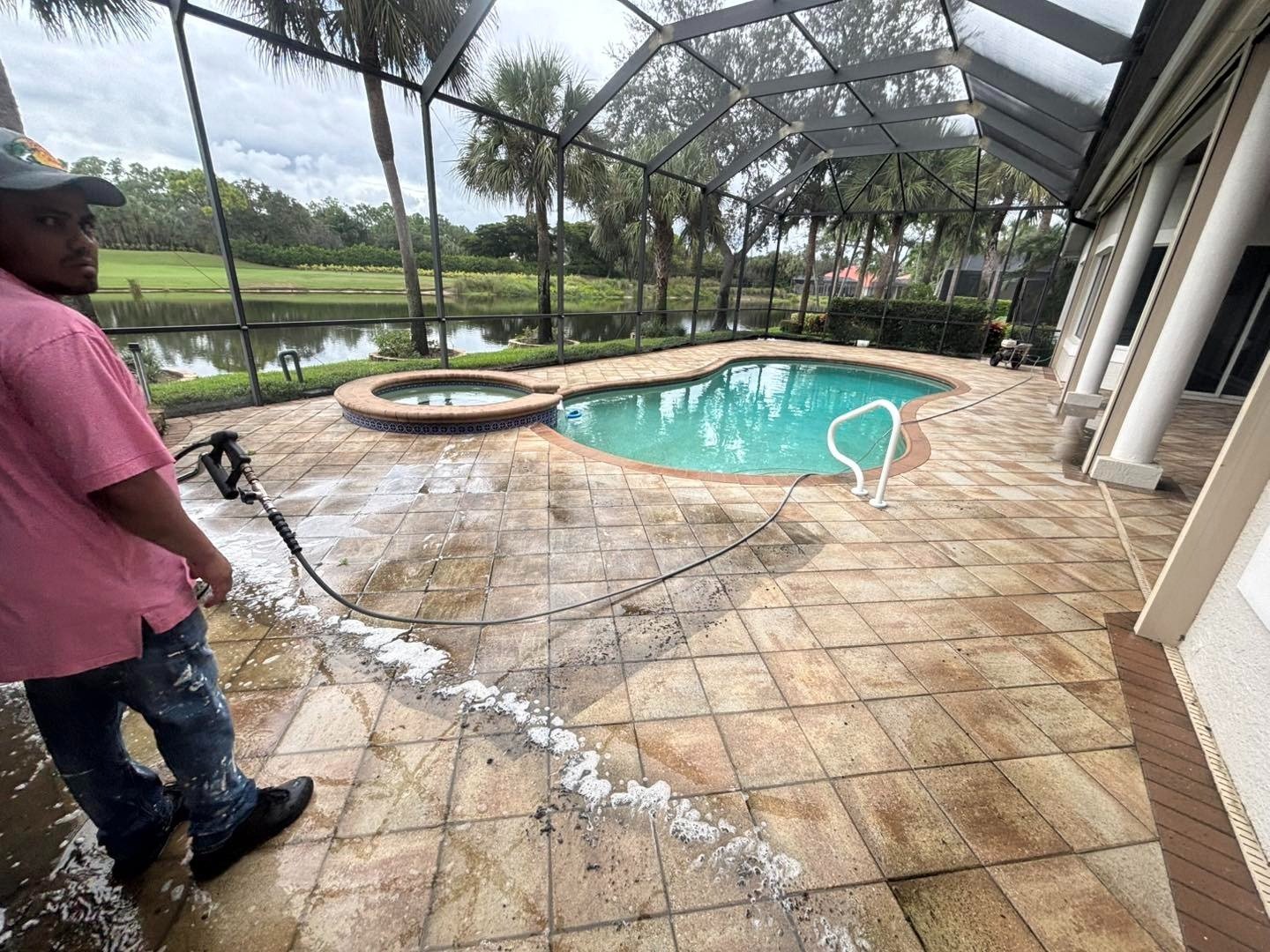 Worker holding a cleaning wand beside a pool and foamy tiled deck