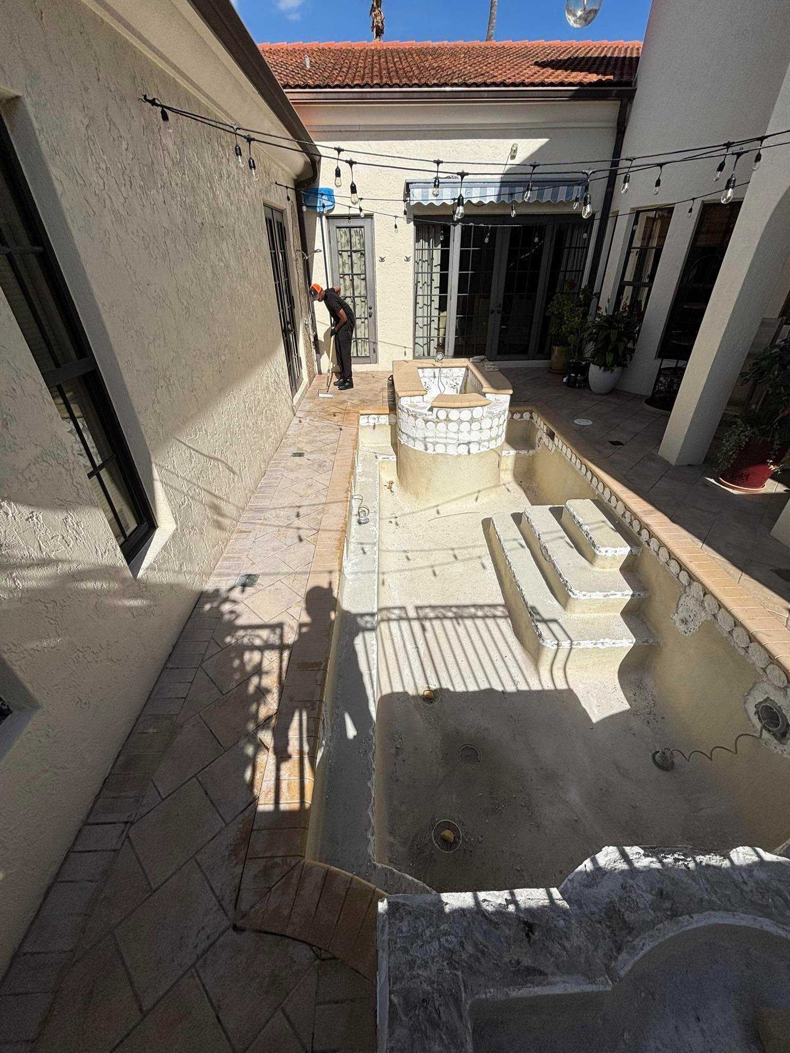 Worker beside an empty courtyard pool beneath string lights