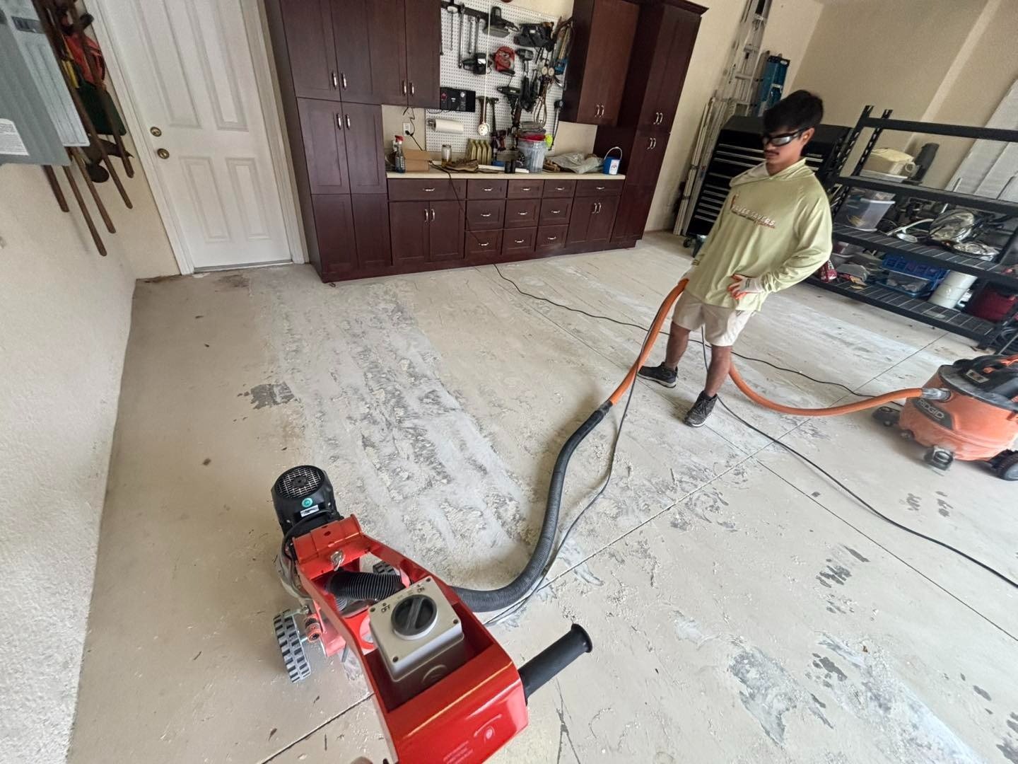 Worker guiding a floor grinder connected to a vacuum hose