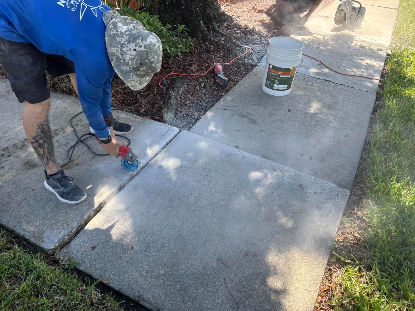 Worker using a handheld grinder along a concrete sidewalk joint