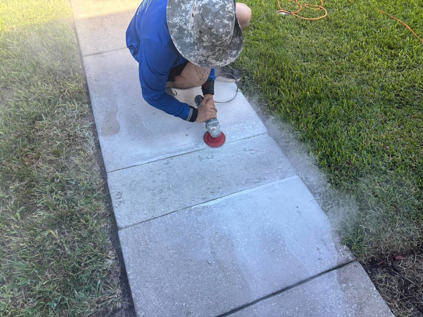 Worker grinding a concrete sidewalk slab beside a strip of grass