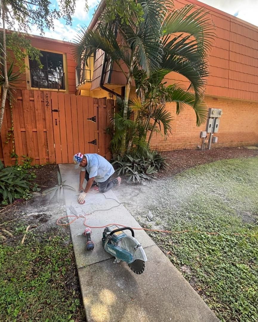 Worker grinding a narrow concrete walkway beside an orange wall and fence