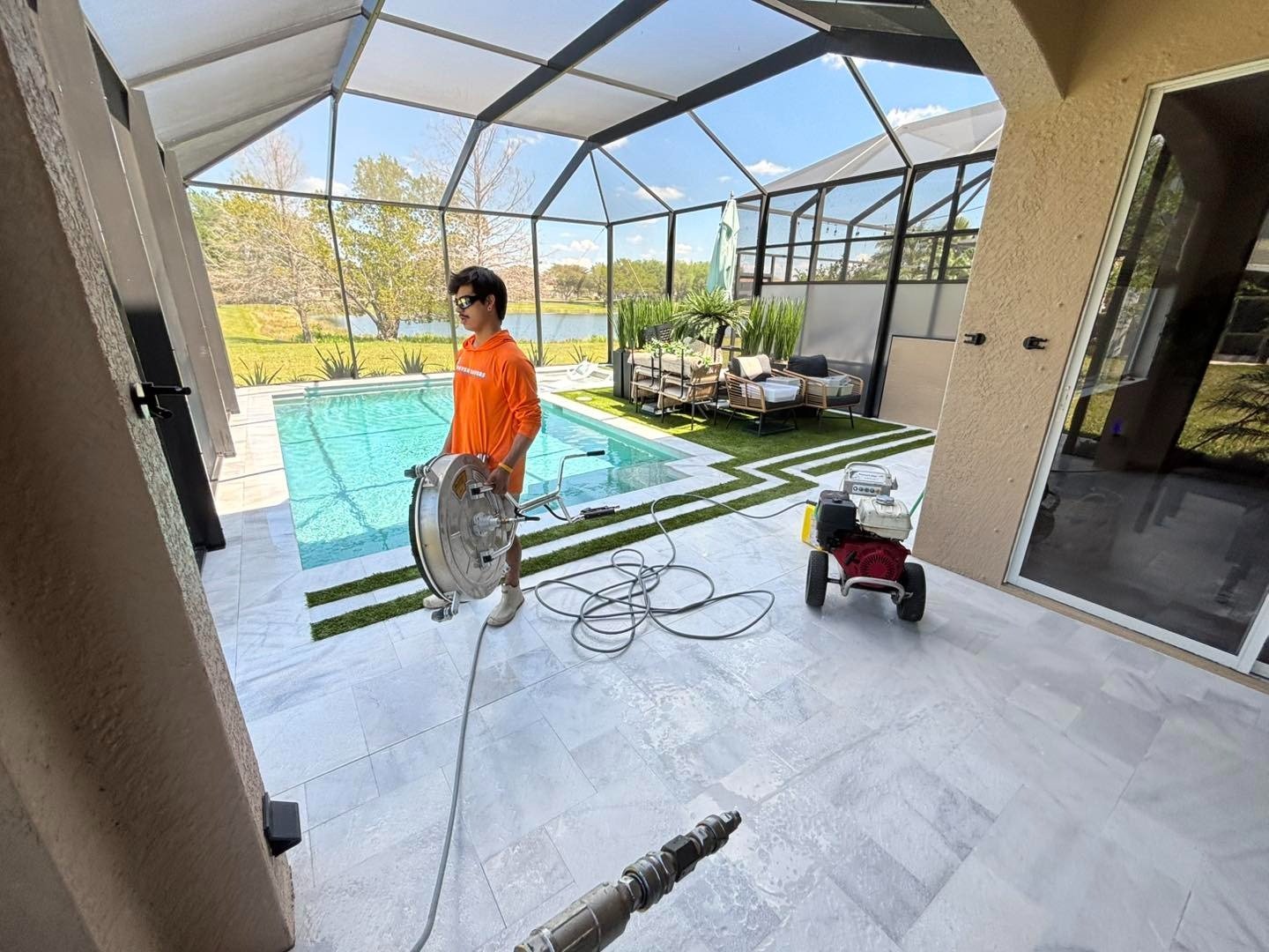 Worker holding a hose on a pale patio beside a screened pool