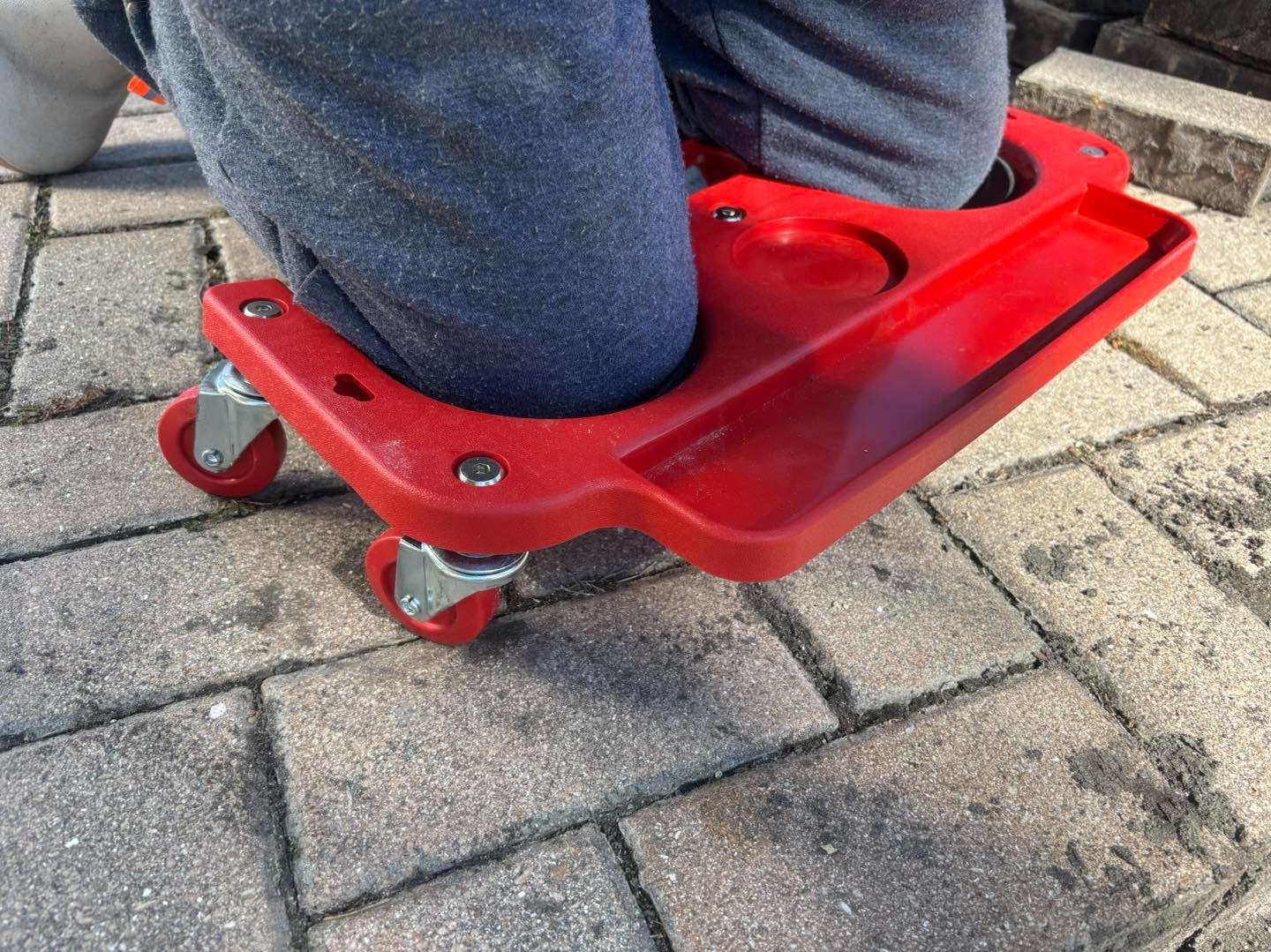 Worker kneeling on a red wheeled seat over pavers