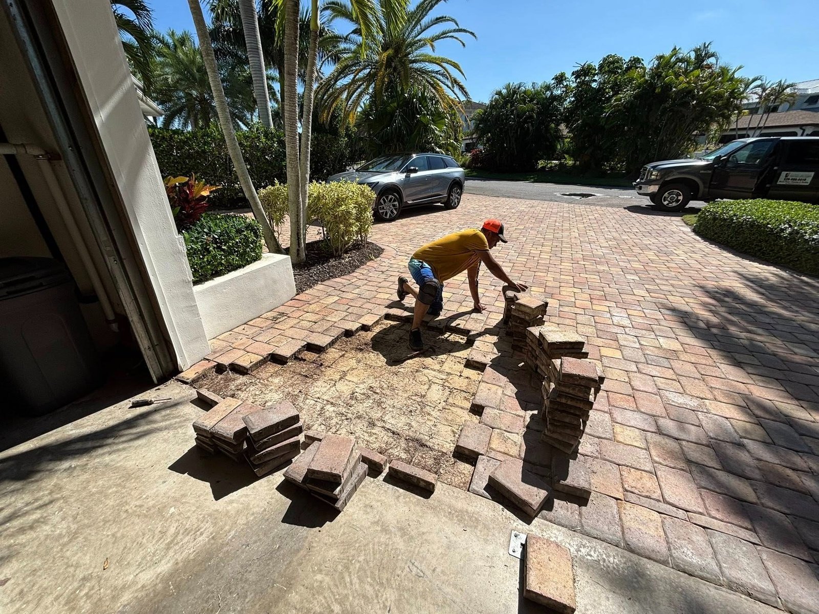 Worker lifting driveway pavers beside an open garage and stacked blocks