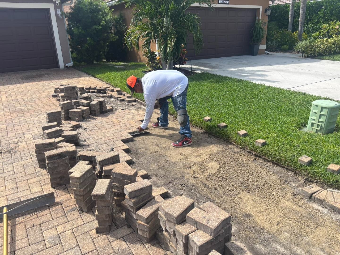Worker lifting pavers along a driveway beside the lawn