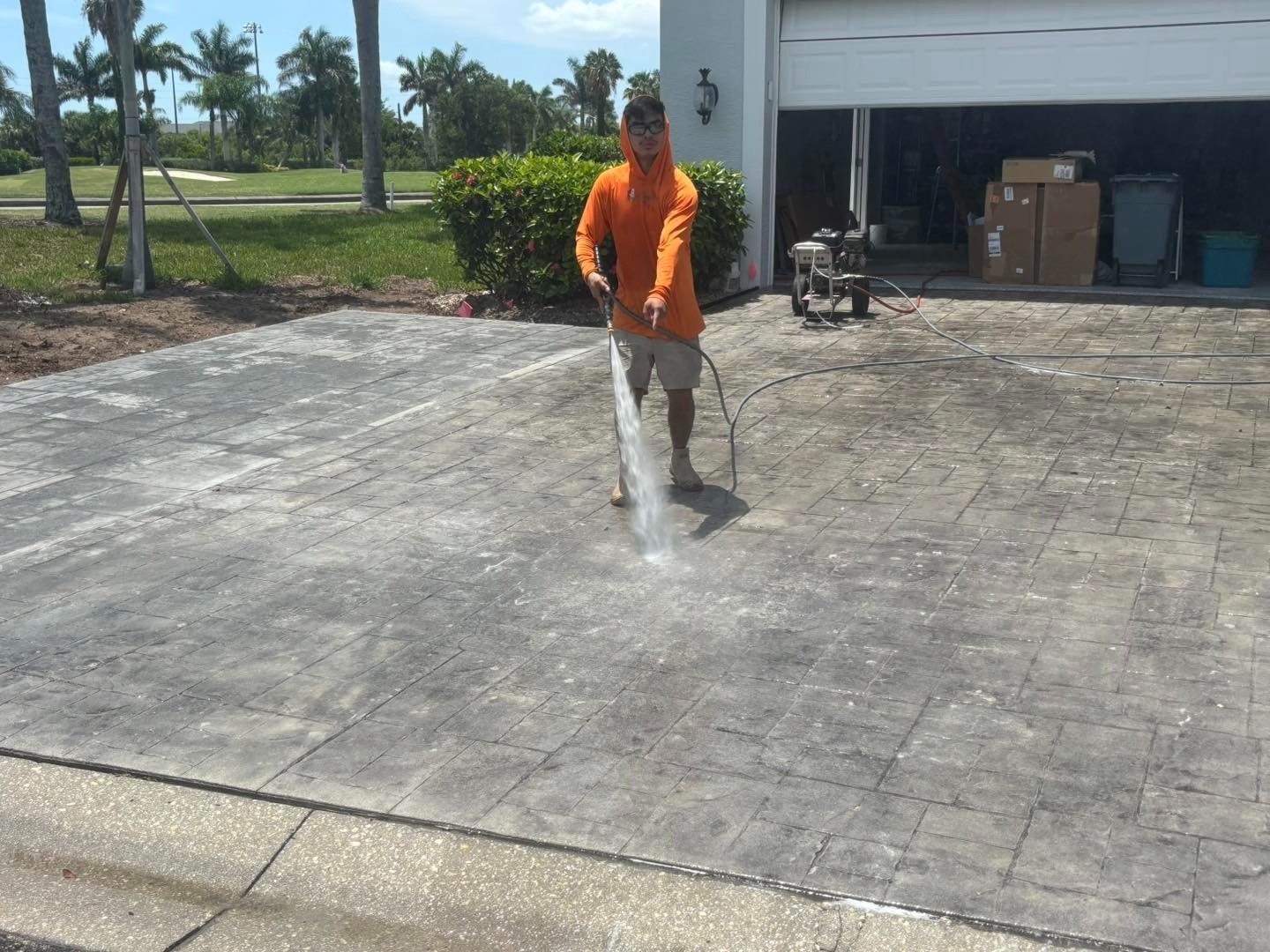 Worker pressure washing a gray patterned driveway in front of an open garage