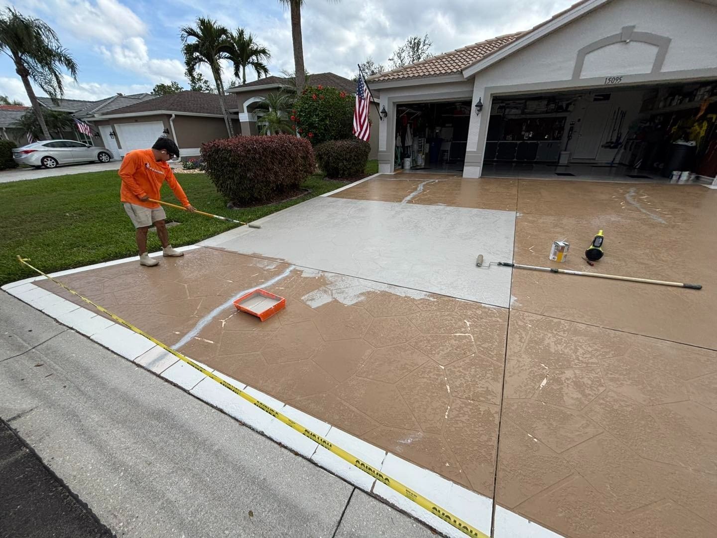 Worker rolling a pale coating across a brown driveway
