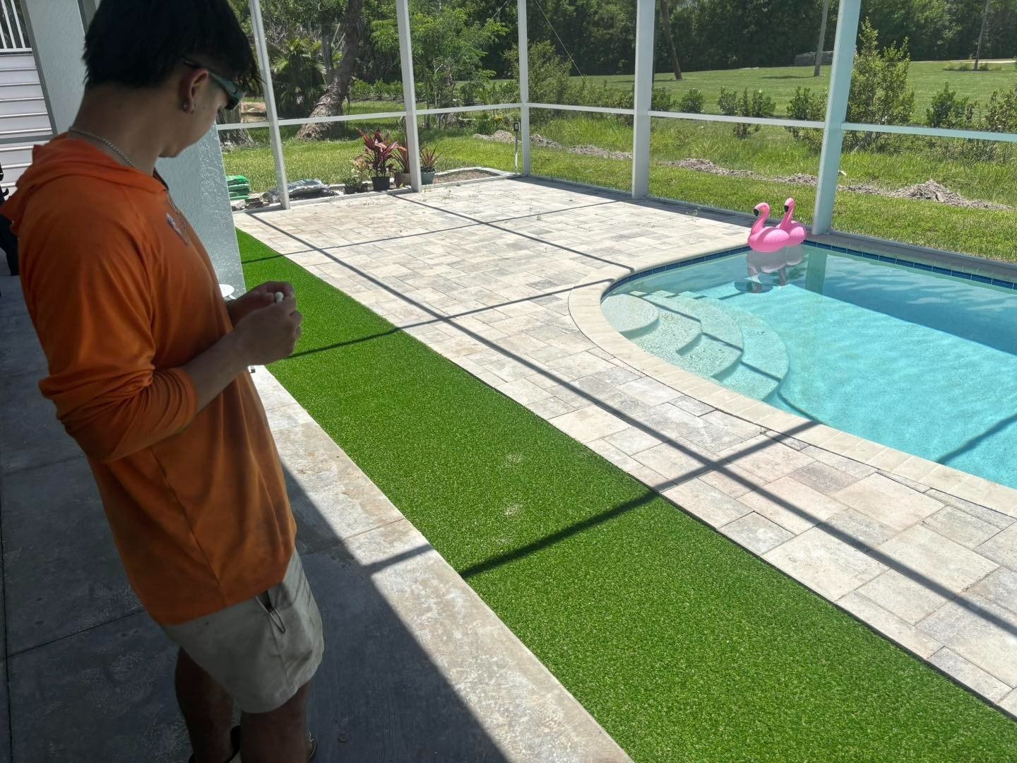 Worker standing beside a screened pool with pale pavers and green turf
