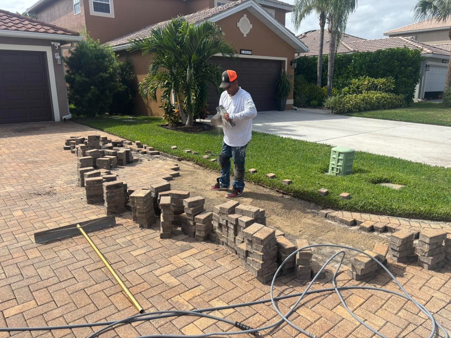 Worker standing beside stacked pavers and an open section of driveway