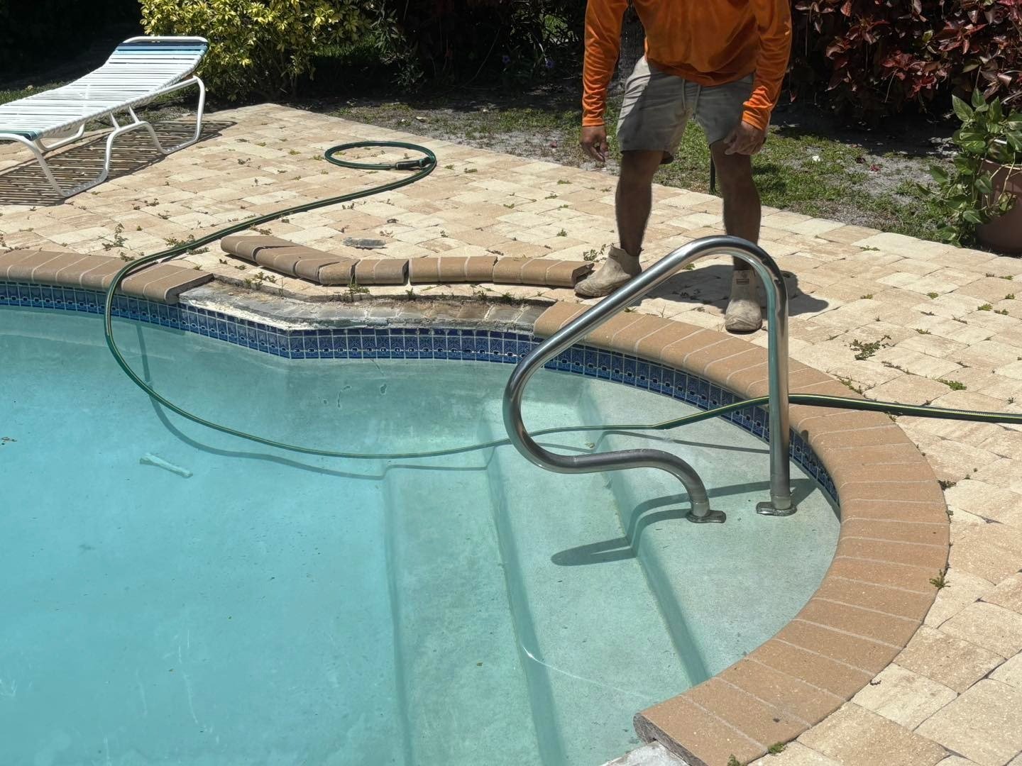 Worker standing beside lifted pool coping and a metal entry handrail