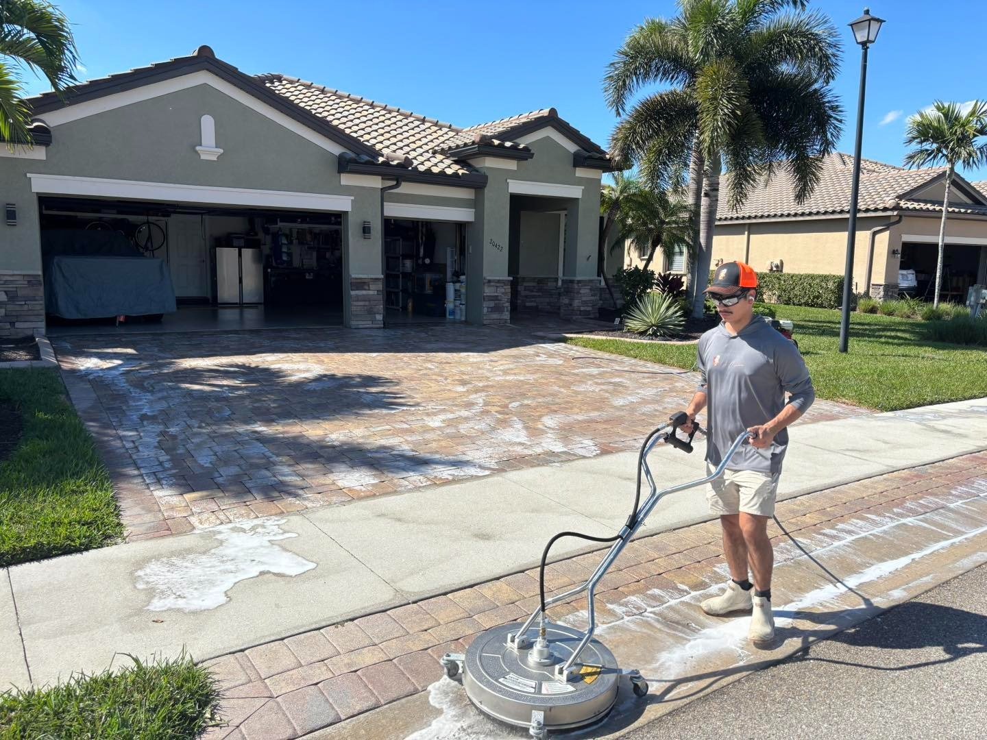 Worker operating a surface cleaner on a residential paver driveway