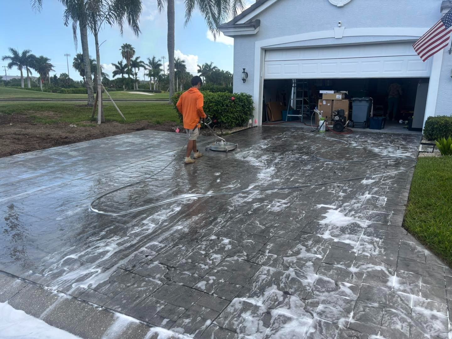 Worker washing a patterned driveway covered with white foam outside a garage