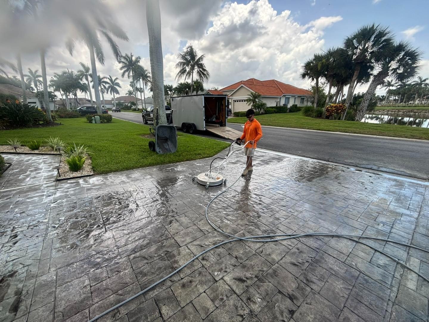 Worker washing a wet patterned driveway near the street and work trailer