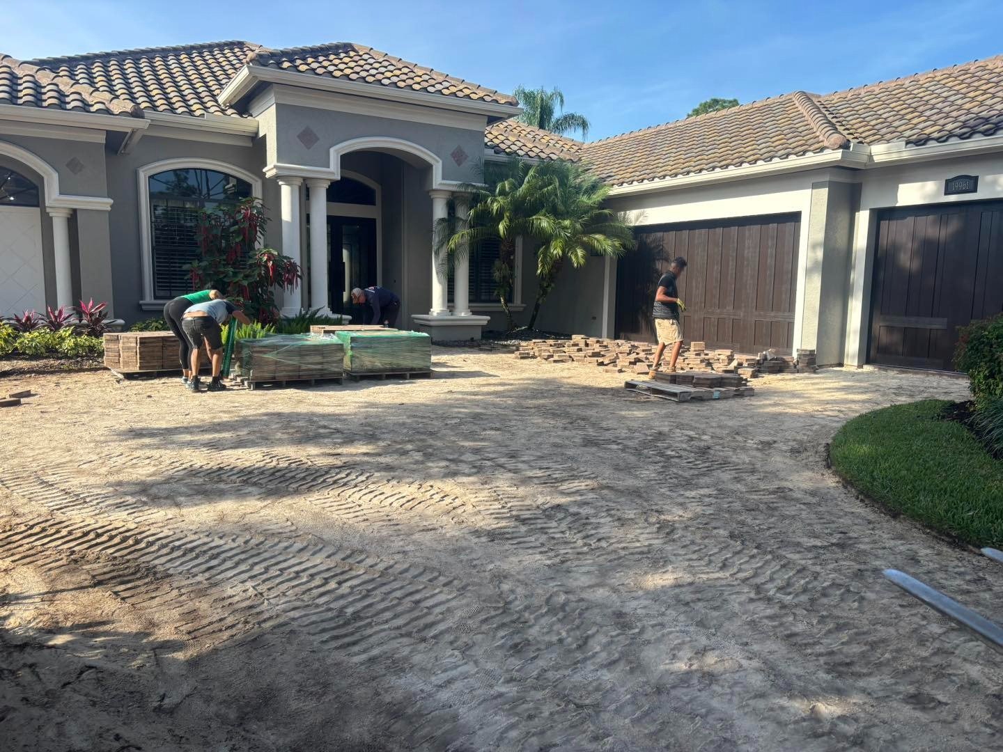 Workers on exposed driveway base outside a house with dark garages