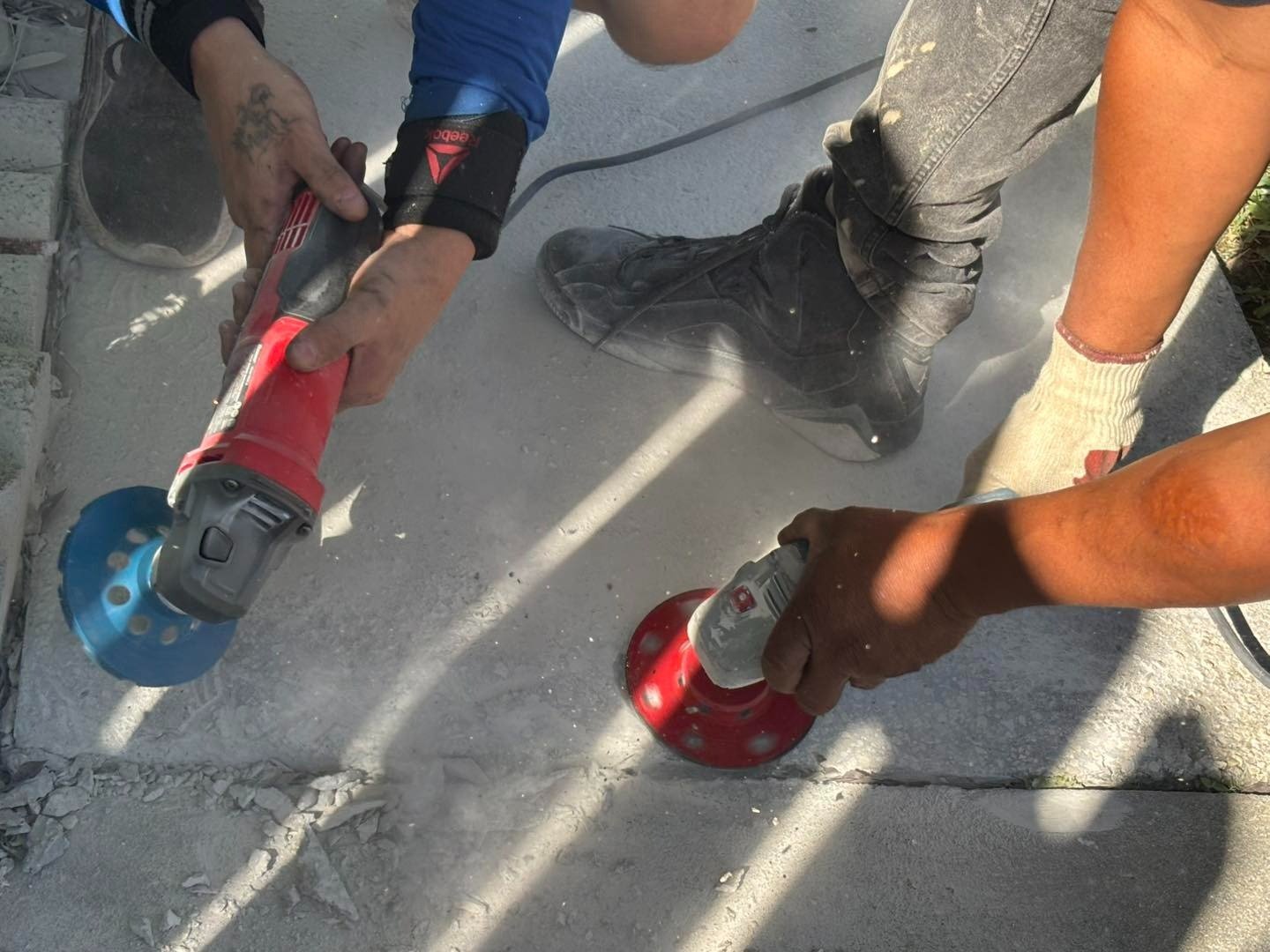 Workers using handheld tools on a concrete surface beside a joint