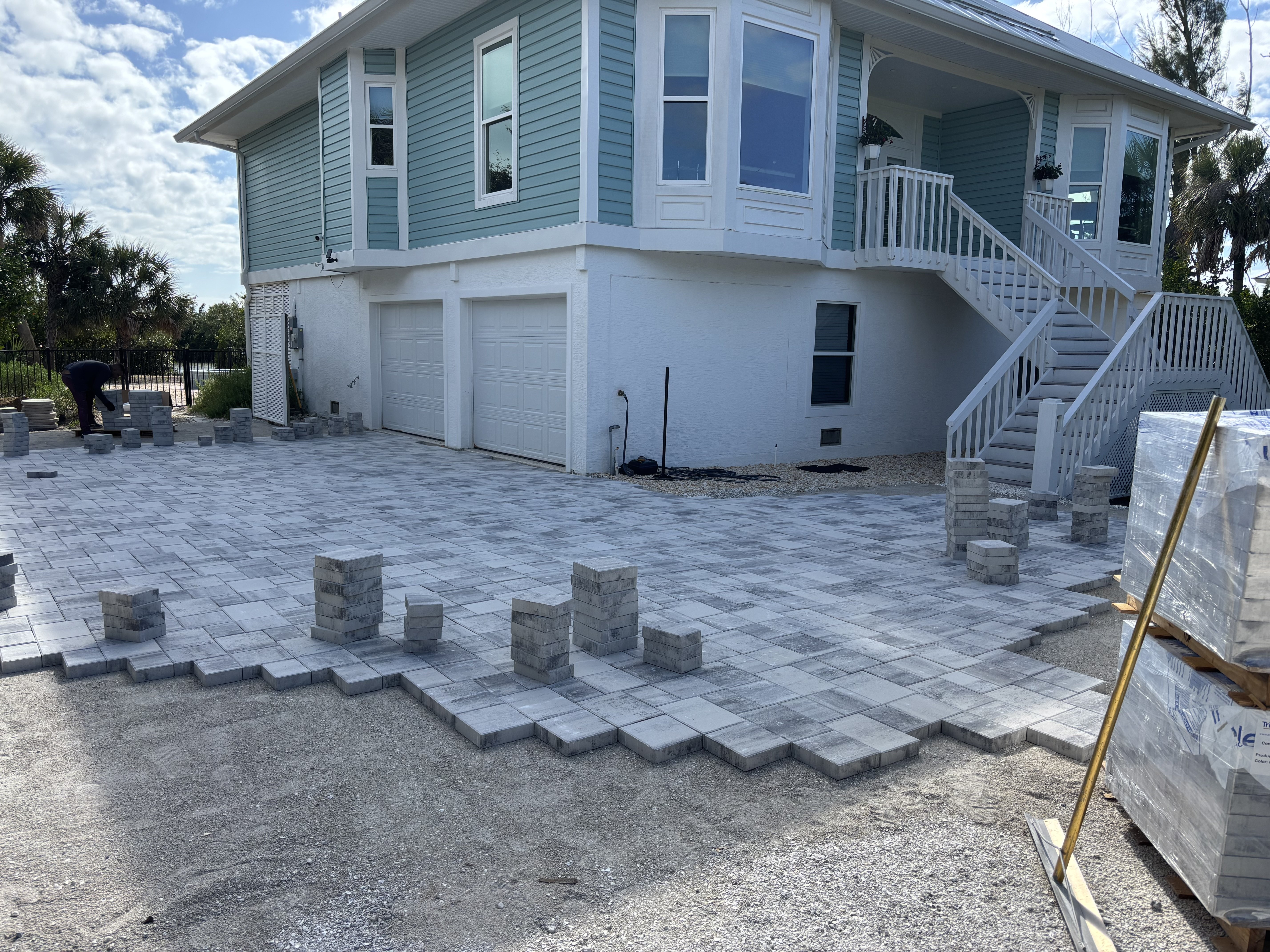 Partly laid gray driveway pavers outside an elevated house with exterior stairs