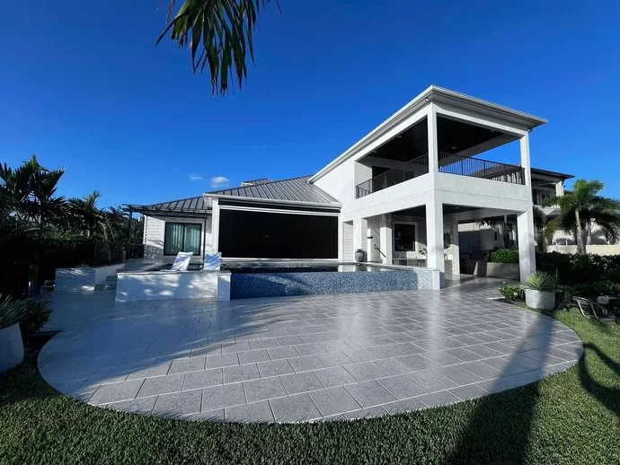Wide pale pool deck outside a two-story waterfront home under blue sky