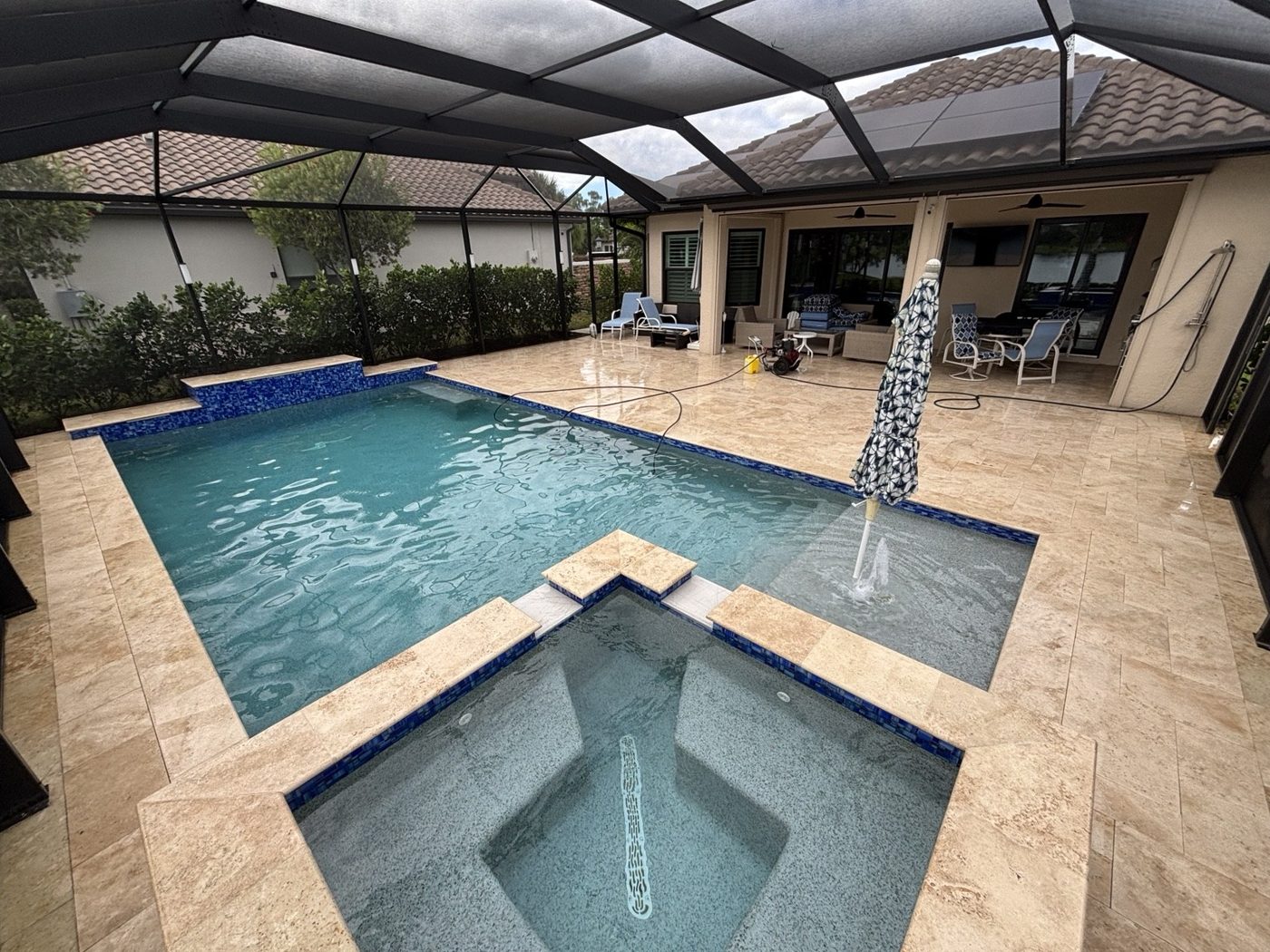 Travertine deck surrounding a screened pool and spa in Estero, Florida