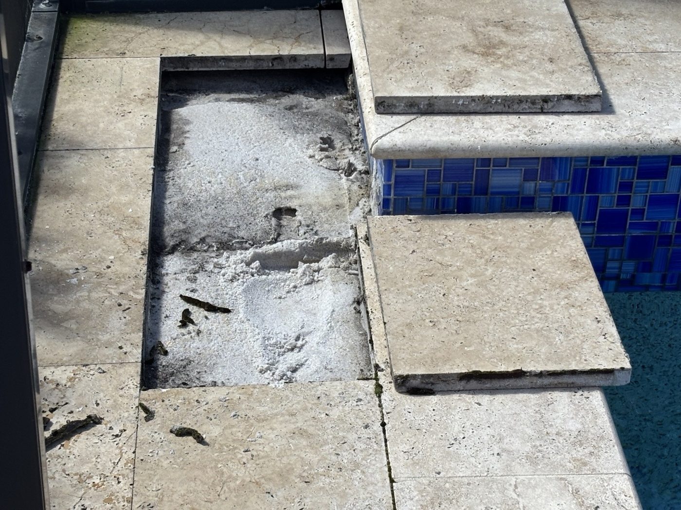 Lifted travertine stones exposing the area beneath poolside paving during repair in Estero