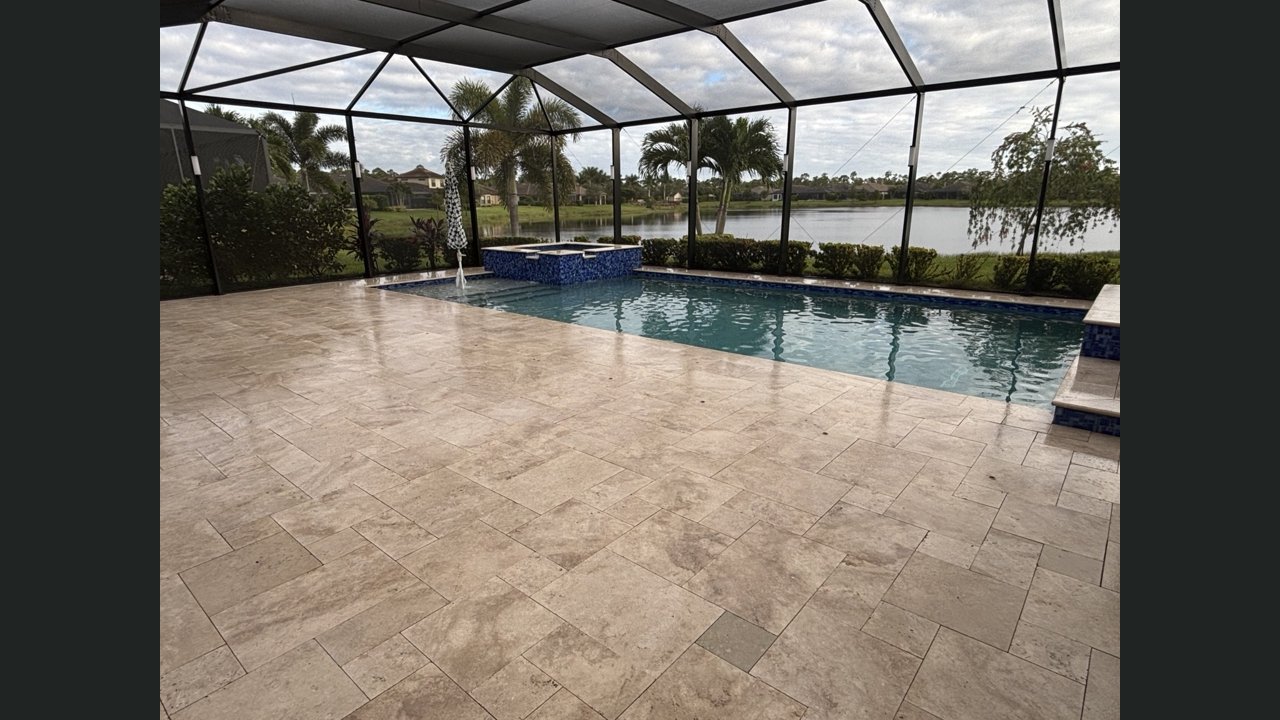 Finished light travertine pool deck beside a screened pool and raised spa in Estero, Florida