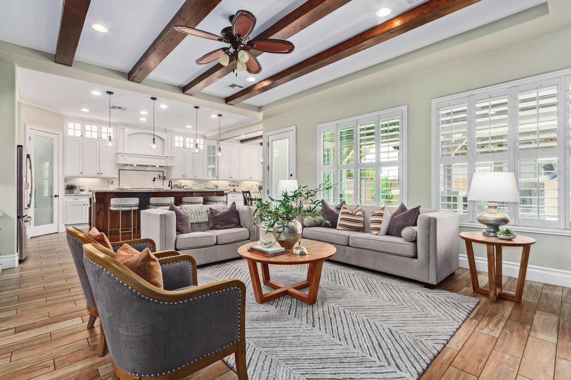 Bright open-plan living room with comfortable seating, wood beams and a white kitchen